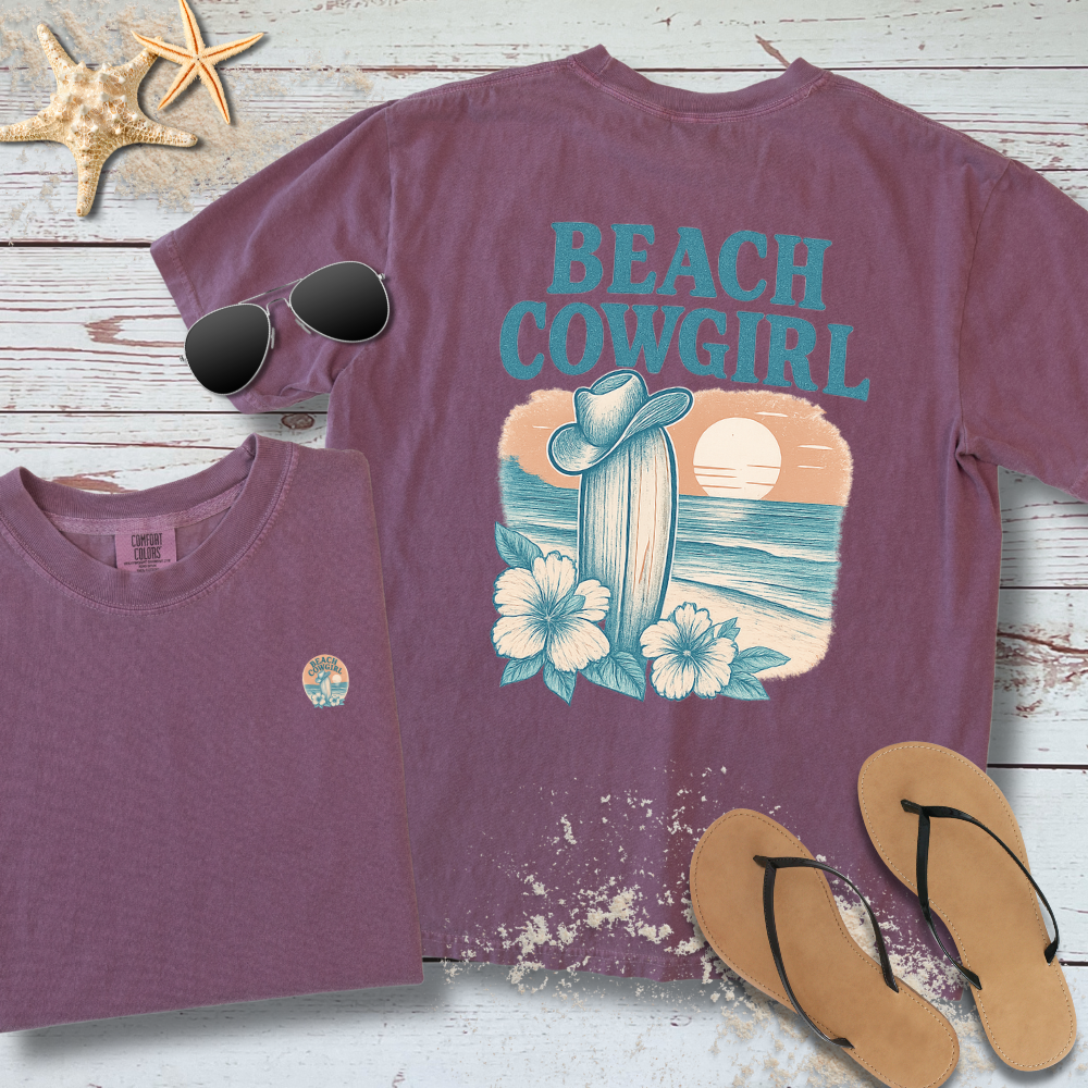 Purple t-shirt with 'Beach Cowgirl' design on a wooden surface with sunglasses and flip-flops.