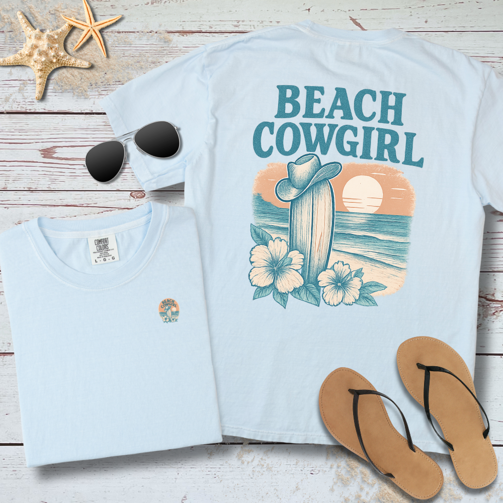 Light blue t-shirt with 'Beach Cowgirl' design on a wooden surface with sunglasses and flip-flops.