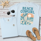 Light blue t-shirt with 'Beach Cowgirl' design on a wooden surface with sunglasses and flip-flops.