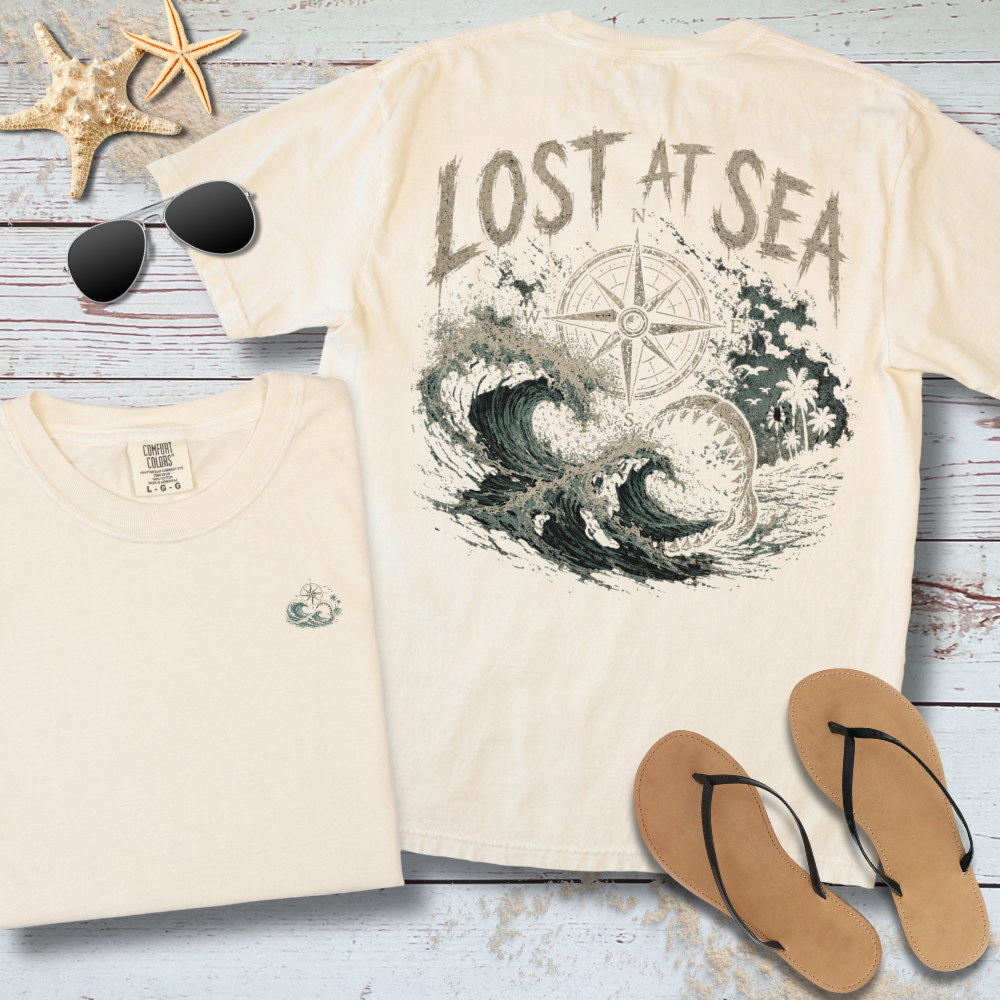 Beige t-shirt with 'Lost at Sea' design, sunglasses, starfish, and flip-flops on a wooden surface.