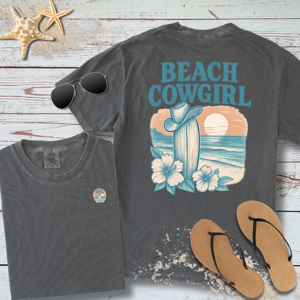 Gray t-shirt with 'Beach Cowgirl' design on a wooden surface with sunglasses and flip-flops.